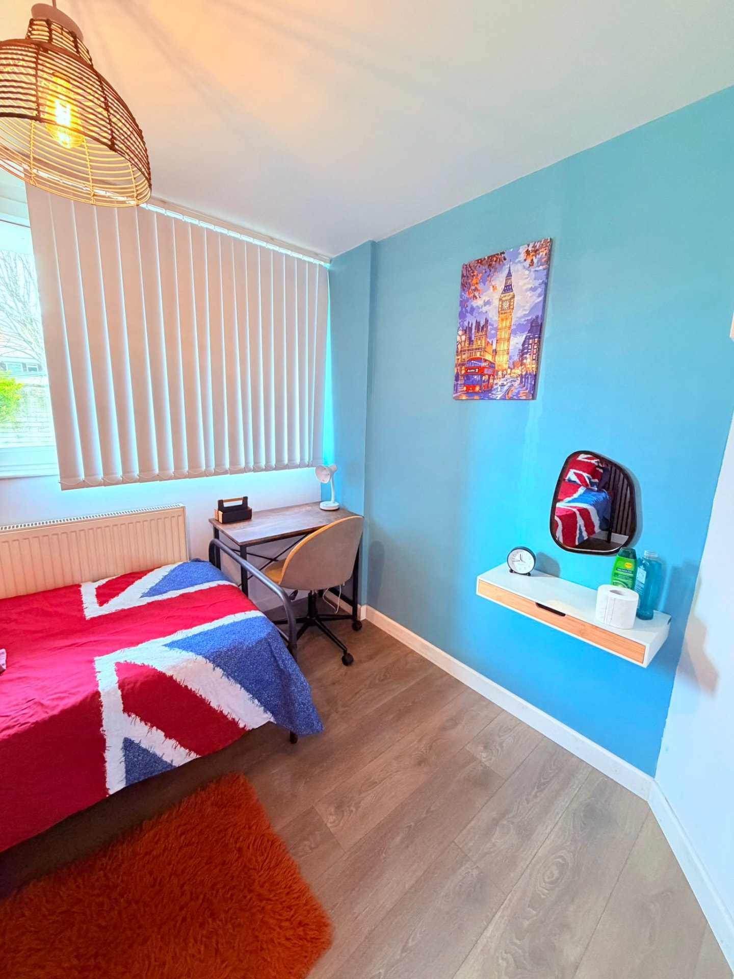 Bright blue bedroom with study desk, lamp and London artwork